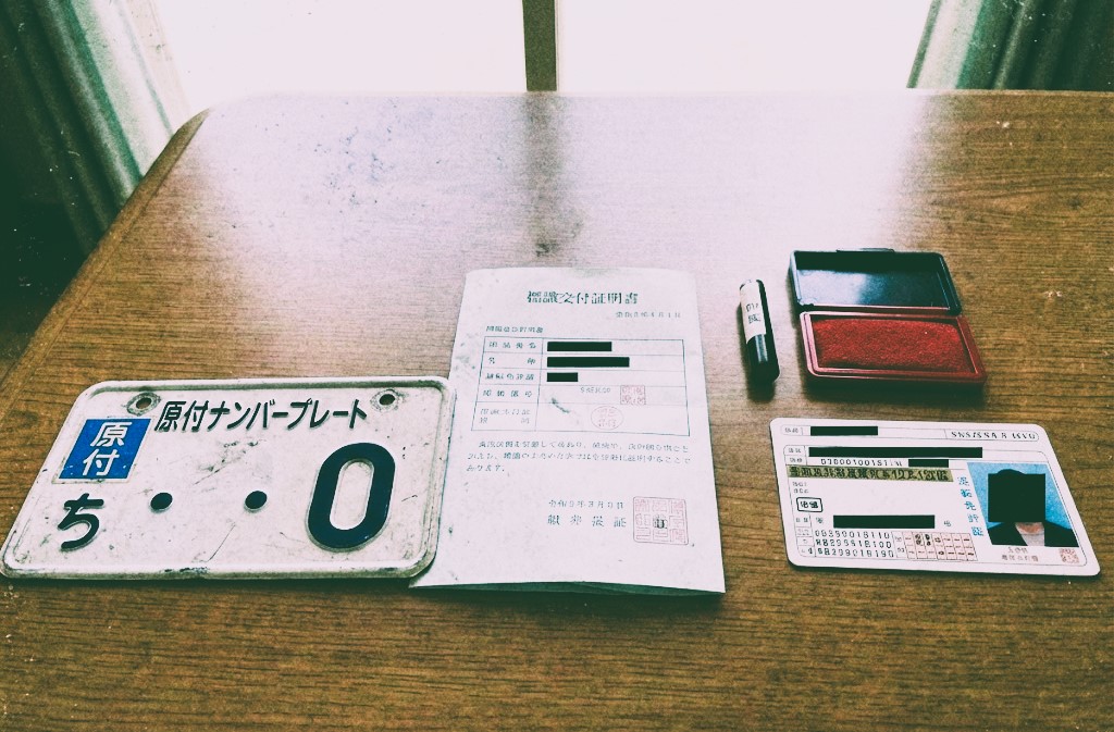 バイク廃車110番|原付を自分で廃車する際の必要書類イメージ。役所窓口へ持参するナンバープレート、標識交付証明書、印鑑などを並べた写真。
